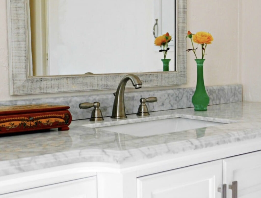 Close up of bathroom sink with marble counter and mirror behind it.