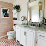 Bright bathroom with brick floor and wood panel wall.