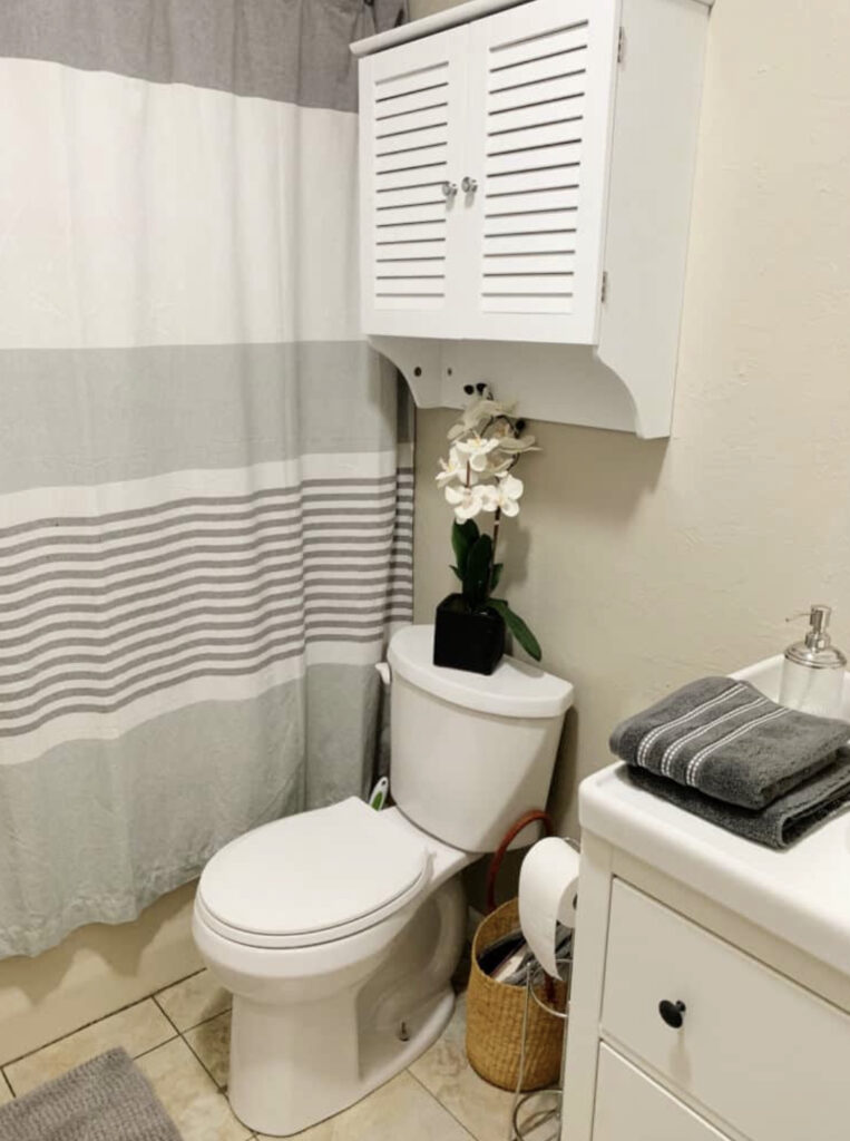 White toilet with an orchid on top and stripe shower curtain.