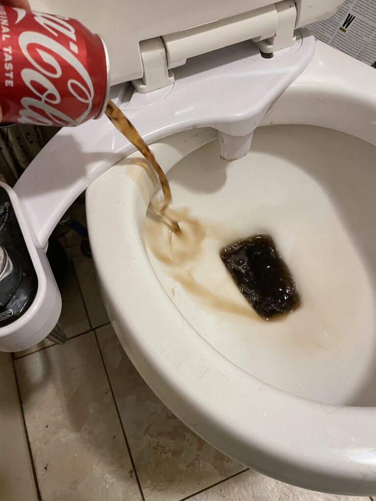 A can of coke being poured into a toilet bowl. 