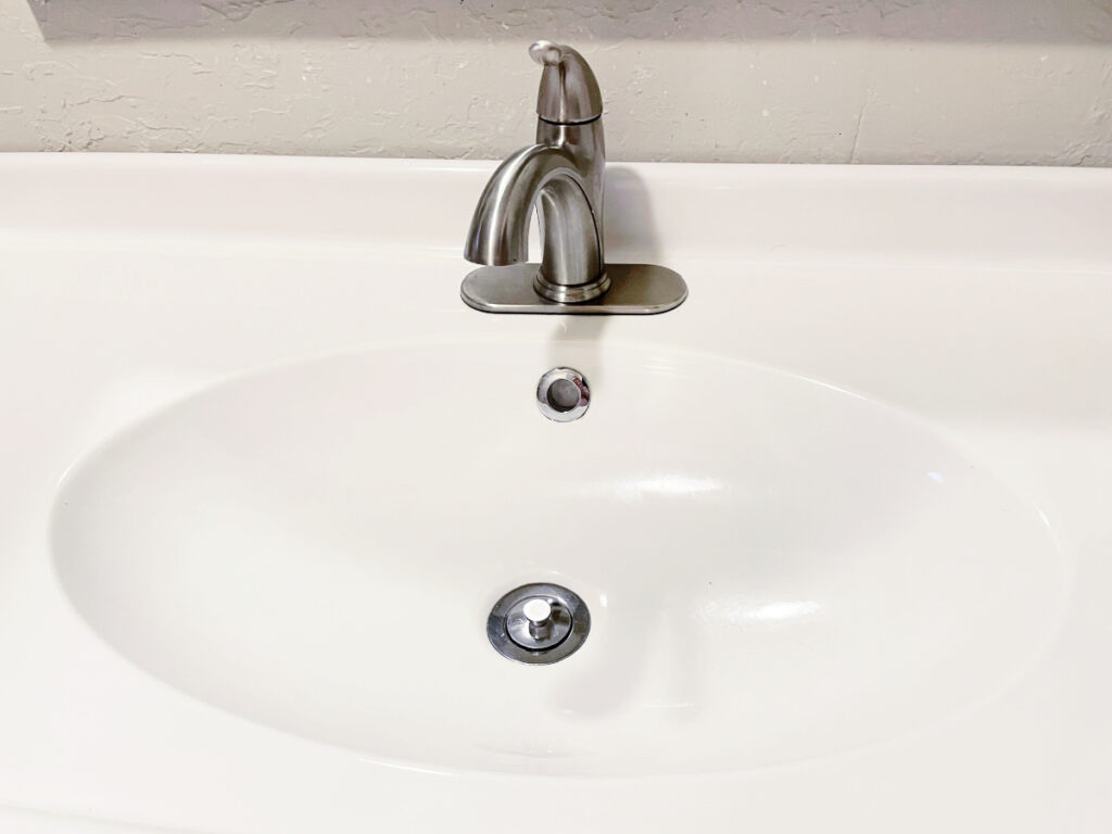 White bathroom sink with a silver faucet and a dirty drain. 