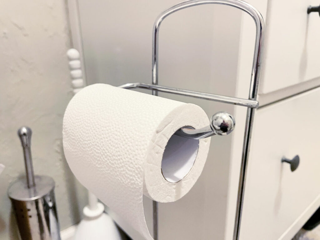 Roll of toilet paper on a holder in front of a bathroom vanity. 