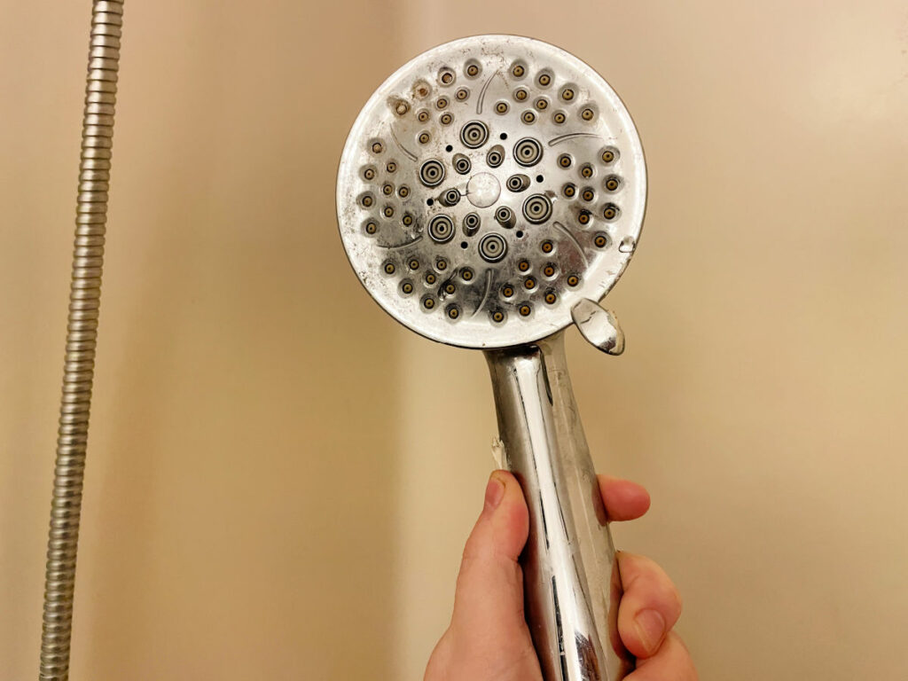 Hand holding a clogged shower head in a walk in shower/ tub combo. 