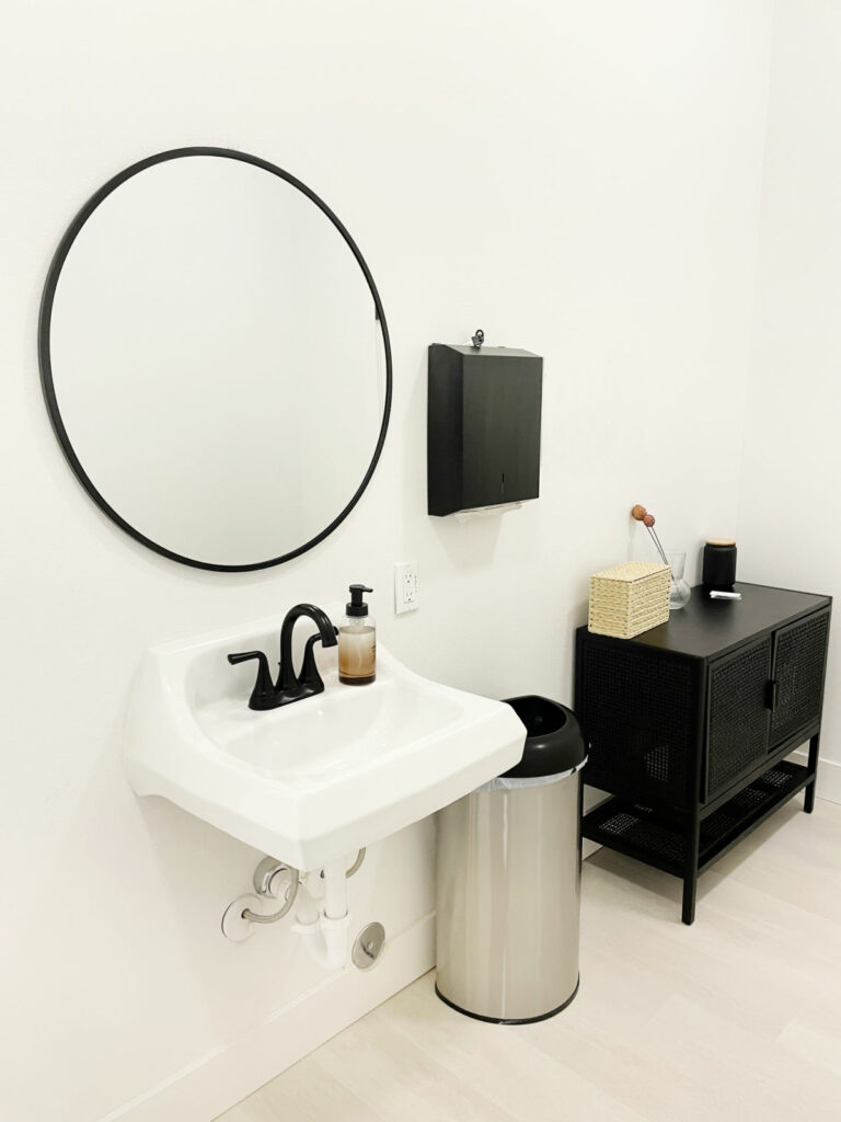 White bathroom with round mirror and black vanity. 