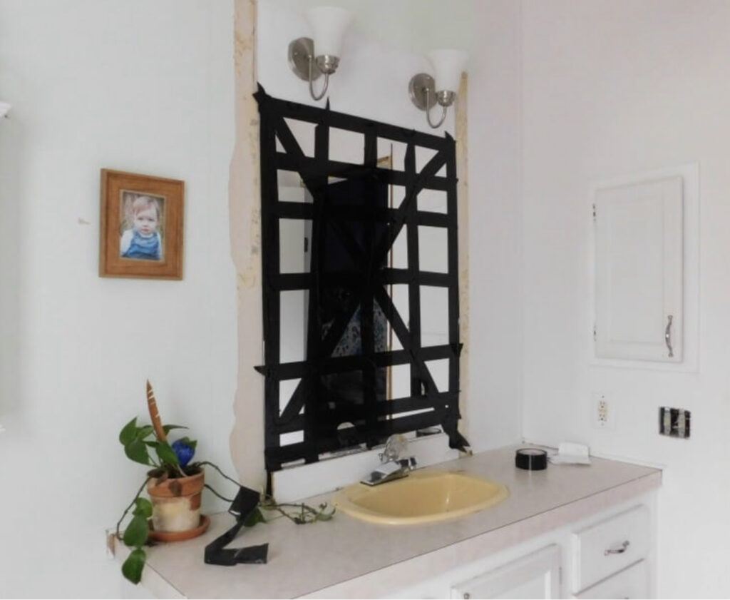 Builder grade mirror with duct tape applied criss cross over it. 