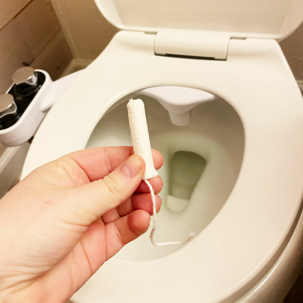 A hand holding a tampon in front of a toilet. 