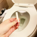 A hand holding a tampon in front of a toilet.