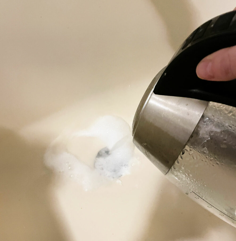 Pouring boiling vinegar down a shower drain with baking soda to deodorize and unclog. 